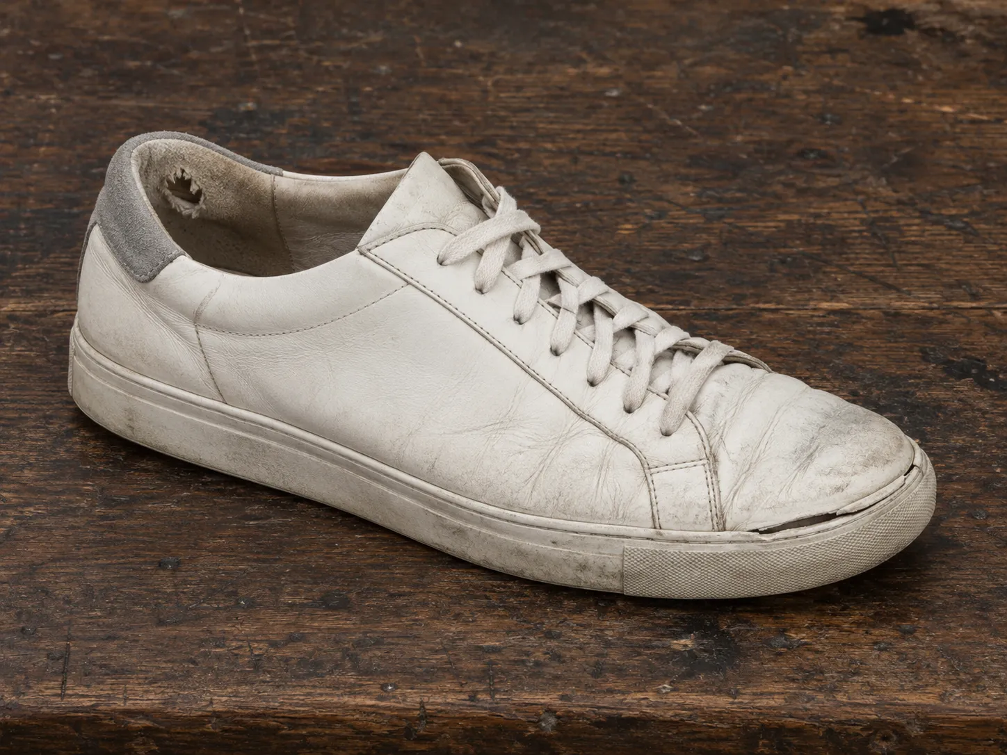 Gedragen witte leren sneaker met een gat in de hielvoering, een zool die bij de neus loslaat en een glad profiel