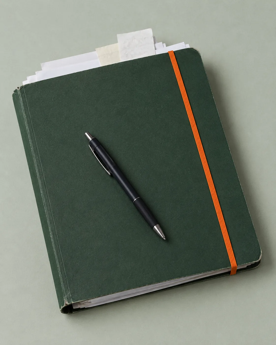 Donkergroene documentenmap met oranje elastiek en een pen op grijsgroen papier