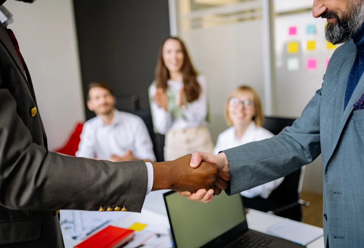 Handdruk na succesvolle bedrijfsovername met contracten op tafel