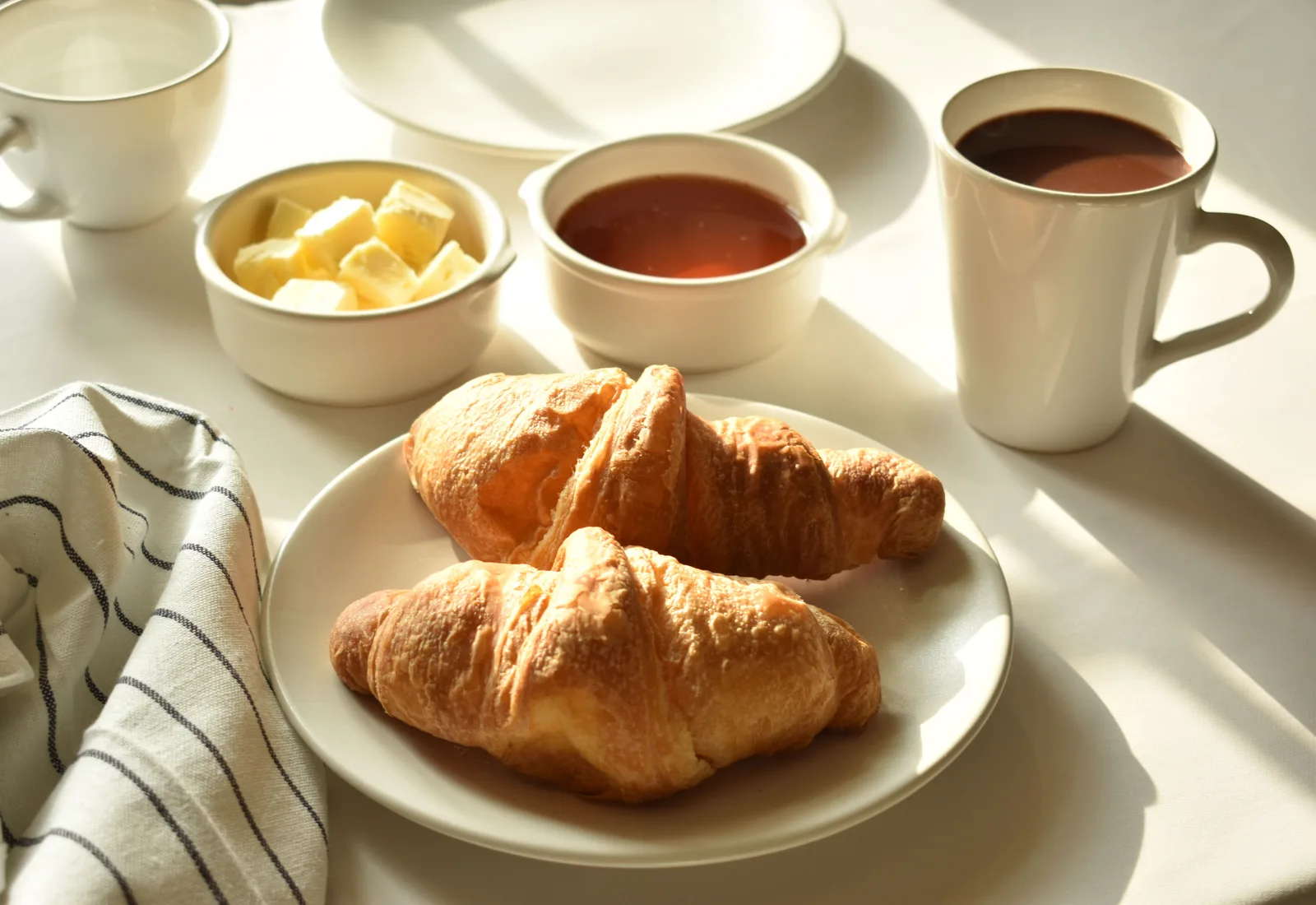 Ontbijttafel met croissants, boter, honing en koffie in ochtendzon