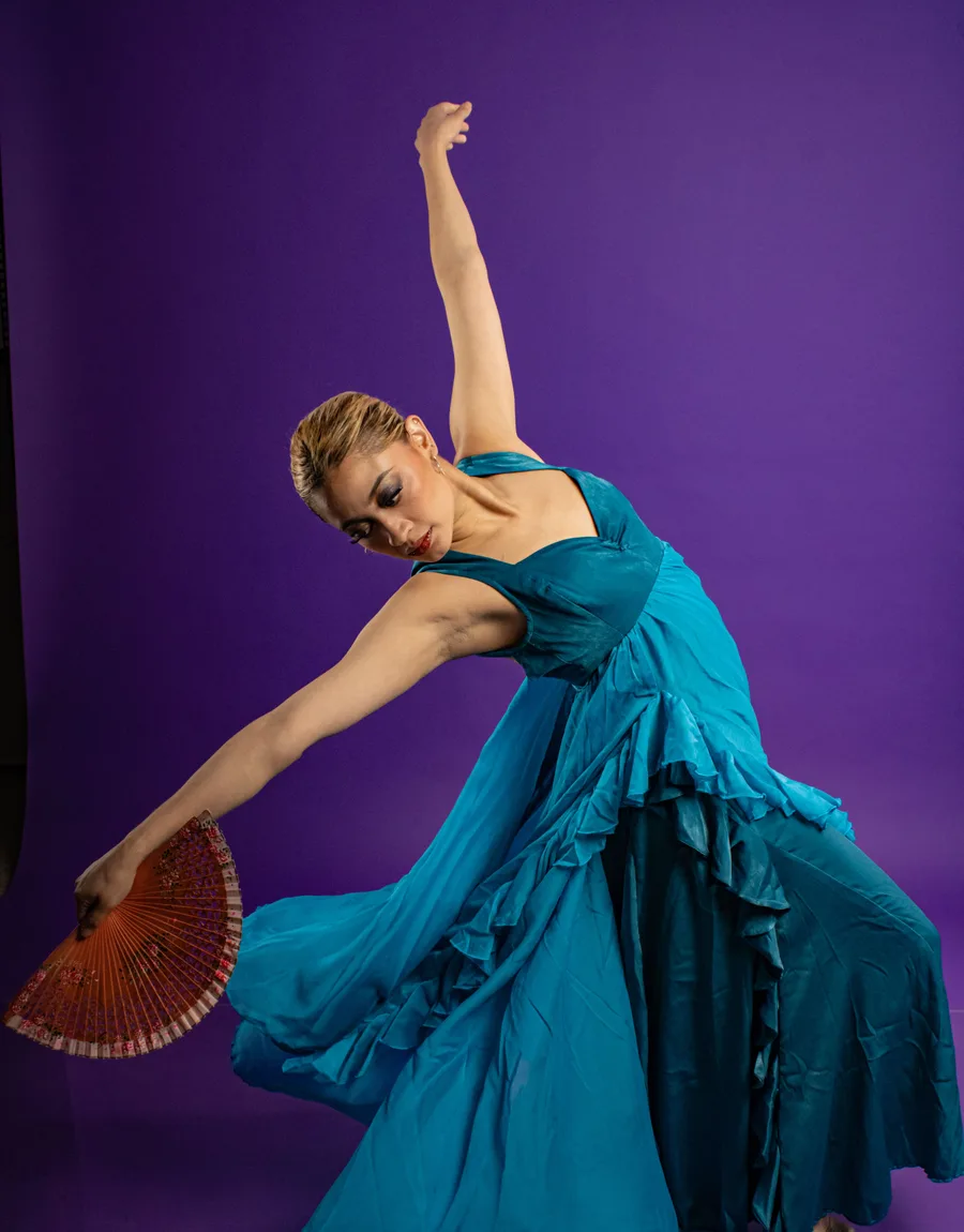 Selena danst met een waaier in een blauwe jurk tegen een paarse achtergrond