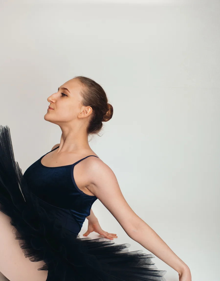 Emma in profiel in donkerblauw balletpak, armen gestrekt naar achteren