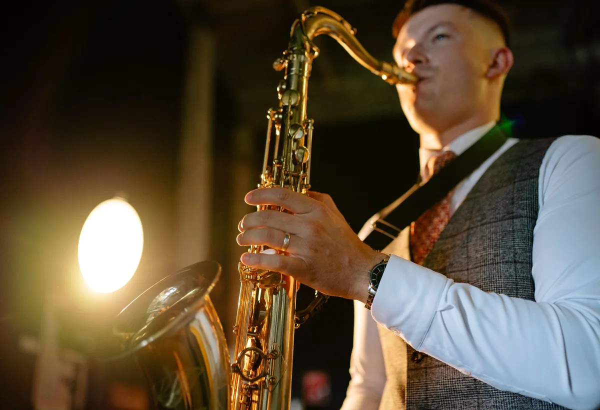 Saxofonist soleert naast de DJ booth op een feest