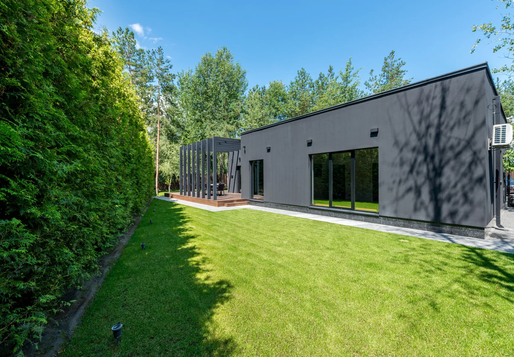 Strak aangelegde achtertuin met gemillimeterd gazon, hoge coniferenhaag en een modern tuinhuis met pergola