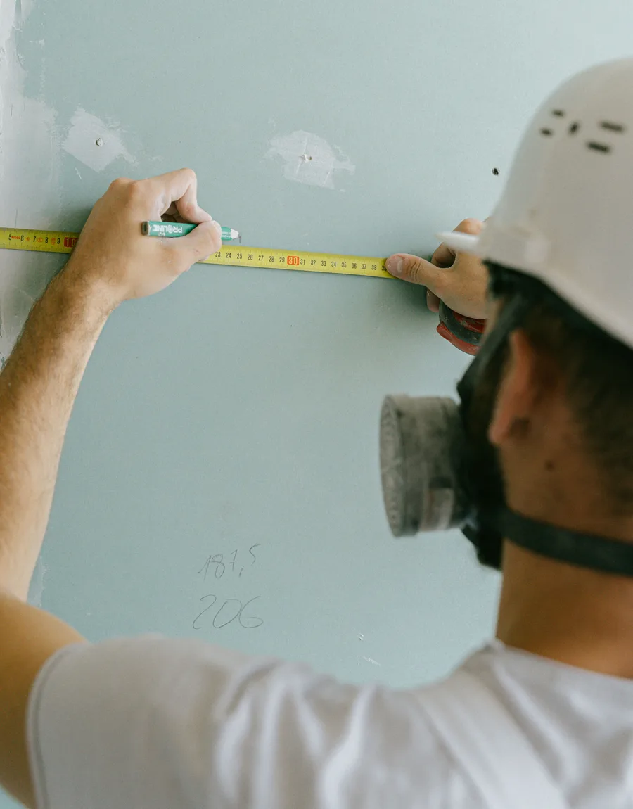 Vakman meet een wand af met duimstok en schrijft maten op de muur