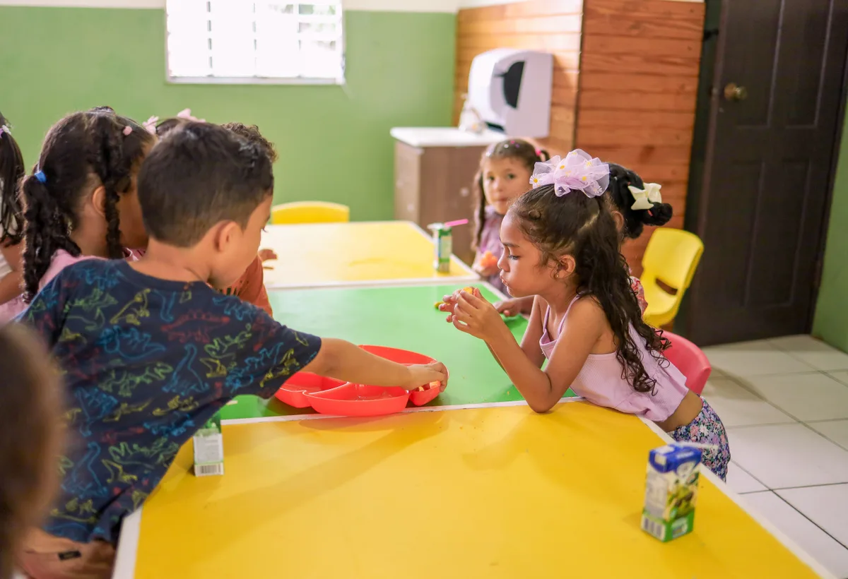 Kinderen eten gezellig samen verse groentepasta aan lage kindertafel