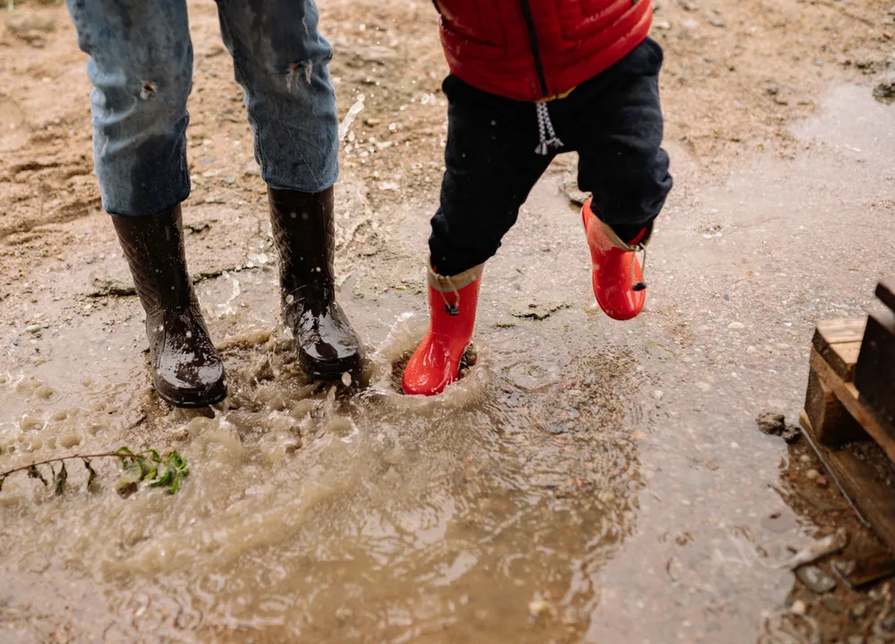 Kind in regenlaarzen springt in een plas