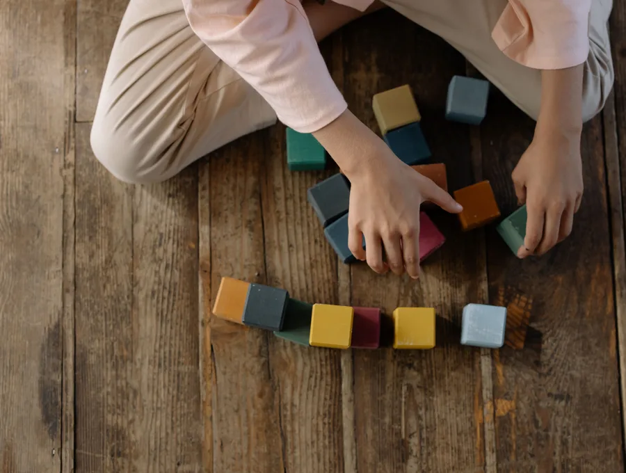 Dreumes bouwt met gekleurde houten blokken op een houten vloer