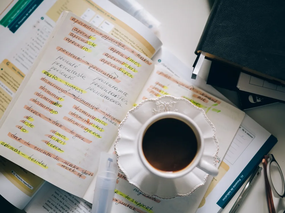 Studieboek met aantekeningen en gele markeerstrepen naast een kop koffie