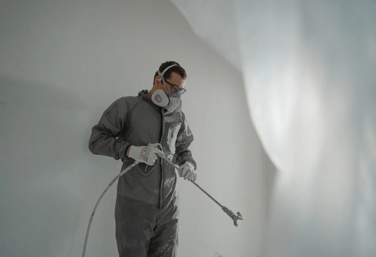 Schilder spuit strakke witte latex op wand met airless spuitpistool