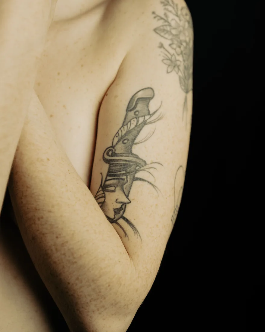 Illustratieve zwart-grijze tattoo van een dolk door een gezicht op een bovenarm