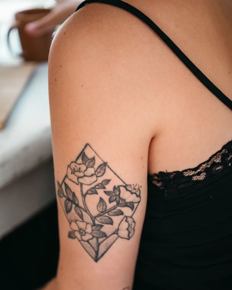 Fijne botanische tattoo van bloemen in een ruitvorm op een bovenarm