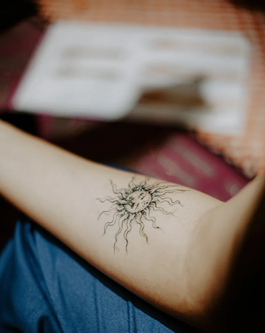 Fine line tattoo van een zon op een onderarm
