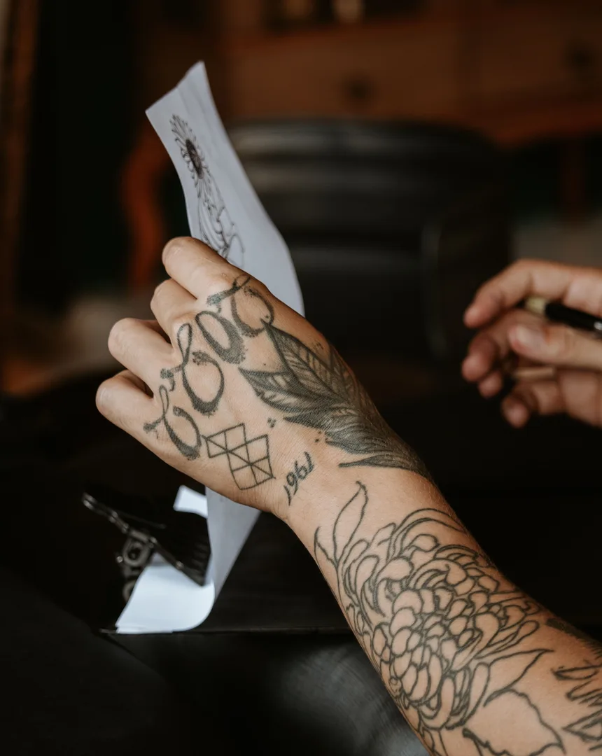 Getatoeëerde hand houdt een tattoo-ontwerp op papier vast