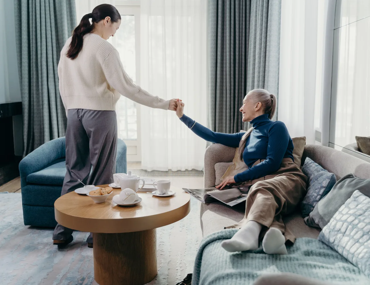 Zorgverlener en een lachende oudere vrouw samen op de bank thuis